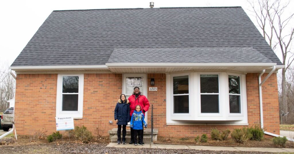 De'Angelo and his sons stand together outside their new home. The full house is in view.