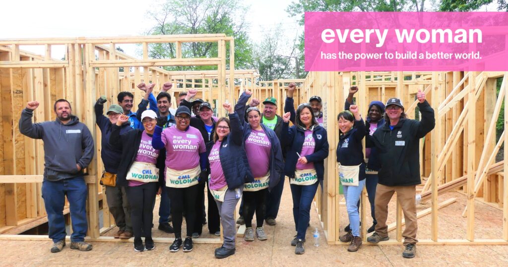 Every woman has the power to build a better world. Volunteers and staff pose for a photo with their hands up in front of the newly framed walls of the house.