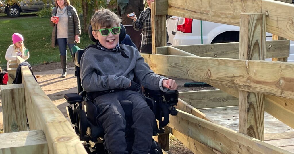 Silas drives his powered wheelchair up his new ramp for the first time with a smile on his face.