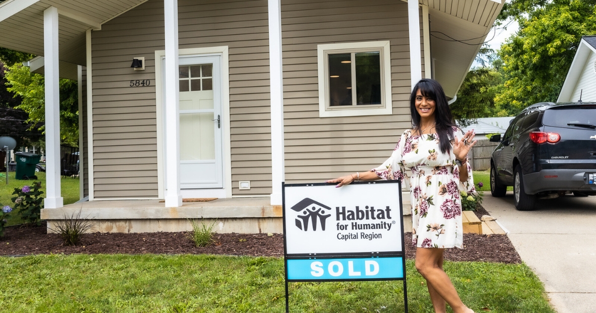 Idalia holds up the keys to her new home out front with the sold sign.