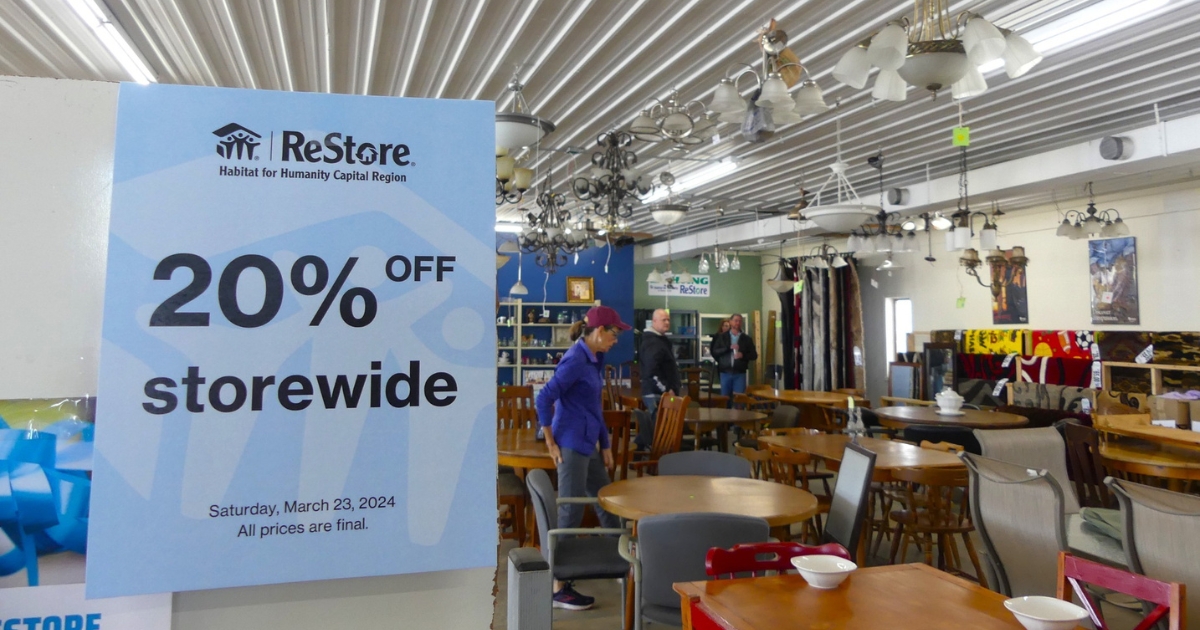 A "20% Off Storewide" poster hangs in the foreground while shoppers peruse the new store layout in the background.