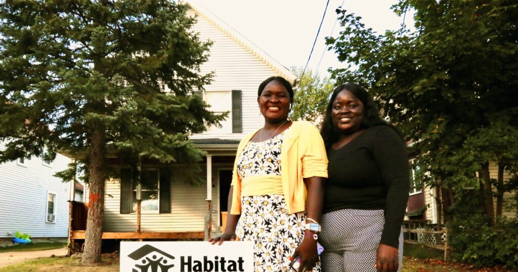 Martha's Home Dedication: Martha and her daughter smile for a photo with a Habitat for Humanity yard sign in front of their future Habitat home.