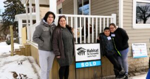 The first homeowner in the neighborhood, Rebellia and her children pose with their sold sign!